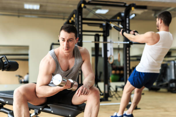 istock Young man sitting and practicing with dumbbells in fitness 1162275442