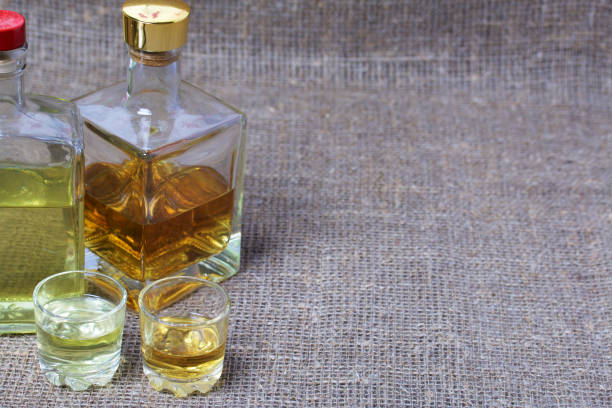 istock Bottled bottles of strong alcohol. From transparent glass, a square form. Near the stack with a drink poured. Against the backdrop of coarse linen fabric. 1162276748