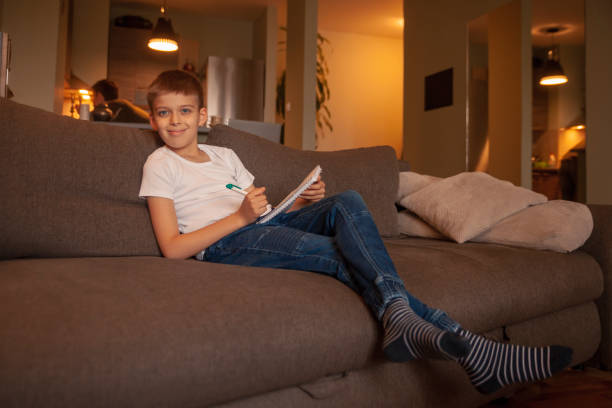 istock Two people, one boy, writing in notebook, while sitting in couch. Man behind in kitchen, out of focus. 1162278339