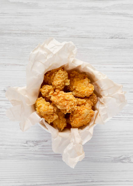 istock Chicken bites in a paper box over white wooden background, top view. Flat lay, overhead, from above. 1162282330