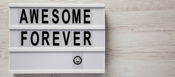 istock 'Awesome forever' words on a lightbox on a white wooden background, top view. From above, flat lay, overhead. Copy space. 1162283066