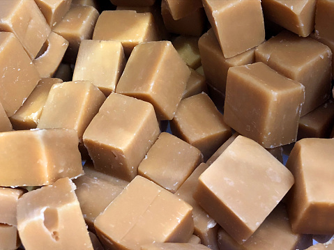 Stock photo of loose squares of soft caramel fudge cubes confectionary being sold at traditional English sweet shop pic and mix, homemade plain Devon Cornish clotted cream fudge candy diced, ready to buy and eat for unhealthy trip at cinema