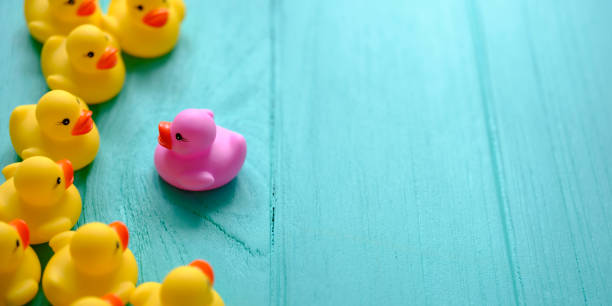 istock Group of yellow rubber ducks gathering around one different purple duck, on a turquoise colored wooden background. 1162285807