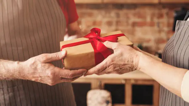 Present of love. Senior man and woman sharing holiday gift at kitchen, panorama, close up