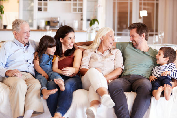 glückliche drei generationen weiße familie sitzt auf einem sofa zu hause und schaut sich an, frontansicht - familie mit mehreren generationen stock-fotos und bilder