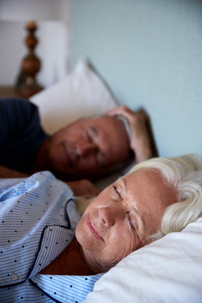 senior white couple asleep in their bed, waist up, close up, vertical - quilt 60s 70s activity imagens e fotografias de stock