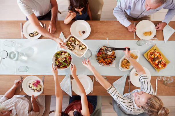 Three generation white family sitting at a dinner table together serving a meal, overhead view Three generation white family sitting at a dinner table together serving a meal, overhead view dining table stock pictures, royalty-free photos & images