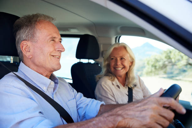 uomo bianco anziano alla guida dell'auto, sua moglie accanto a lui sul sedile anteriore del passeggero, primo piano, vista laterale - driving senior adult car women foto e immagini stock