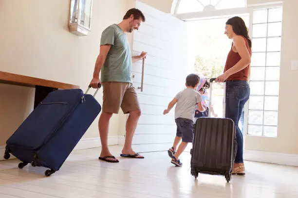 Photo of Mid adult white couple and kids leaving their home with luggage to go on vacation, full length