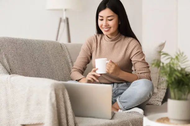 Photo of Happy Girl Relaxing on Comfortable Couch and Using Laptop
