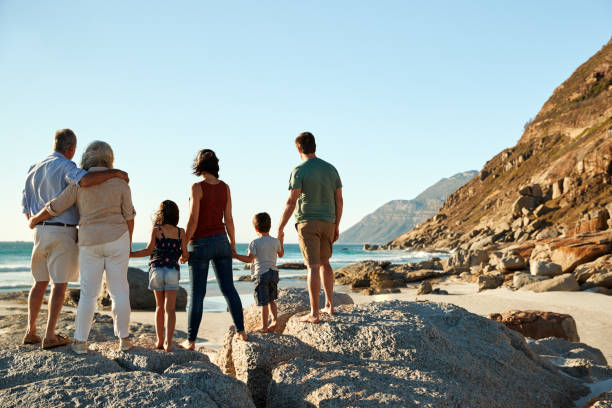istock Three generation white family on a beach stand holding hands, admiring view, full length, back view 1162303165