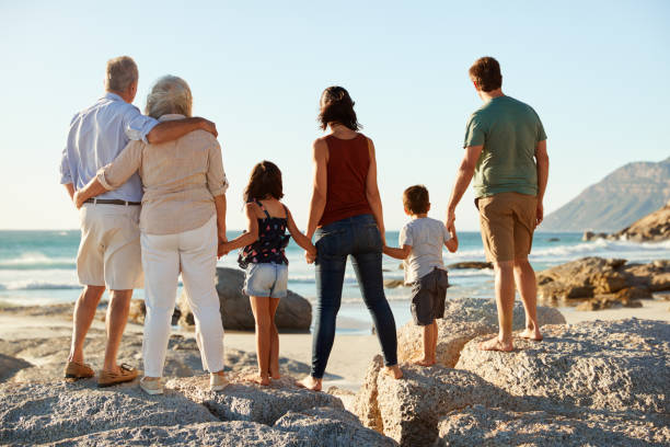 istock Three generation white family on a beach stand holding hands, admiring view, full length, back view 1162303496