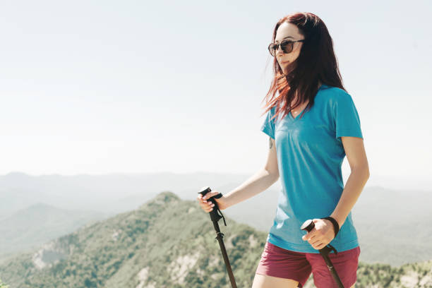 femme sportive marchant avec des poteaux de trekking dans les montagnes d'été. - hiking young women outdoors t shirt photos et images de collection