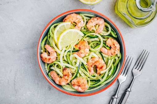 Spiralized zucchini noodles pasta with shrimps on gray stone background, top view