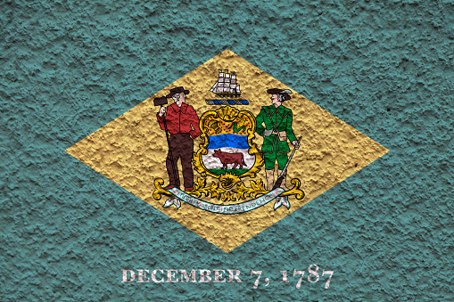 The national flag of the US state Delaware in against a gray wall with stony surface on the day of independence in color of green and yellow. Political and religious disputes, customs and delivery