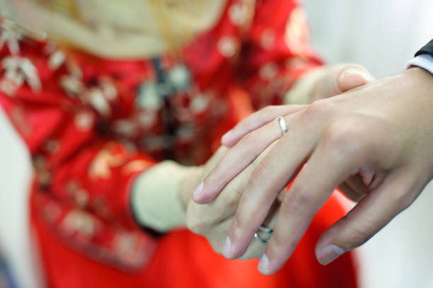 Image of Bride putting wedding ring on grooms finger .
