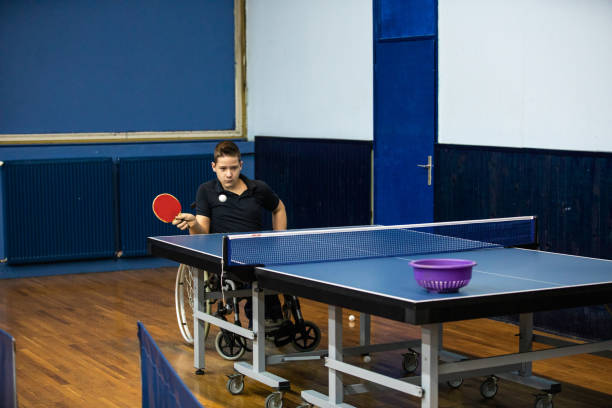 Teenage boy in wheelchair playing table tennis in sports hall, holding racket