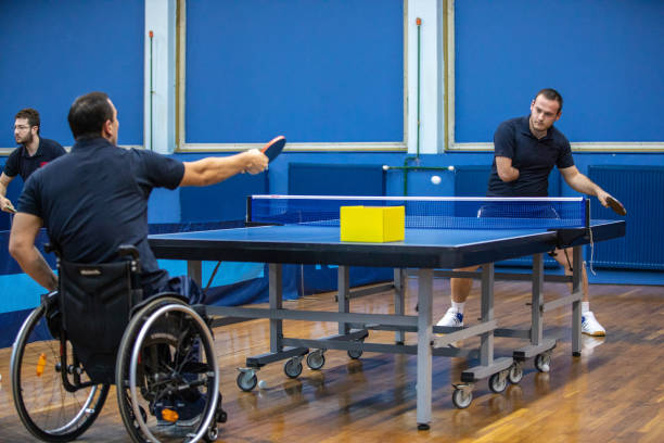 Man in wheelchair against man with amputee hand playing table tennis indoor