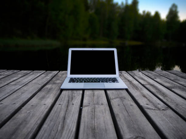 Working with a laptop on a pier, with a forest in the background. This is how we work during the summer in Finland. We use the best technology surrounded by the purest nature.