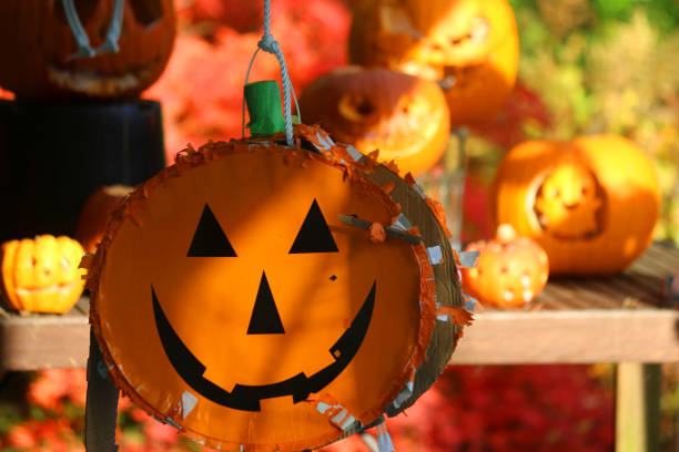 Stock photo of Halloween homemade pinata monster face cardboard / paper arts and crafts, pumpkin pinata party game toy filled with sweets, children's Halloween party games in sunny garden with carved Jack O'lantern pumpkins faces in background, scary hanging imagen de halloween calabaza pinata juego de fiesta juguete lleno de dulces, juegos de fiesta de halloween para niños en el jardín soleado con tallado jack o'lantern calabazas caras en el fondo, colgado aterrador casero pinata monstruo cara cartón / art
