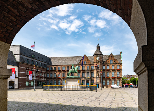 Dusseldorf, Germany - June 25 2019: The Old Town Hall viewed through an arch in Dusseldorf. A van is parked in front and people walk on the cobbles.