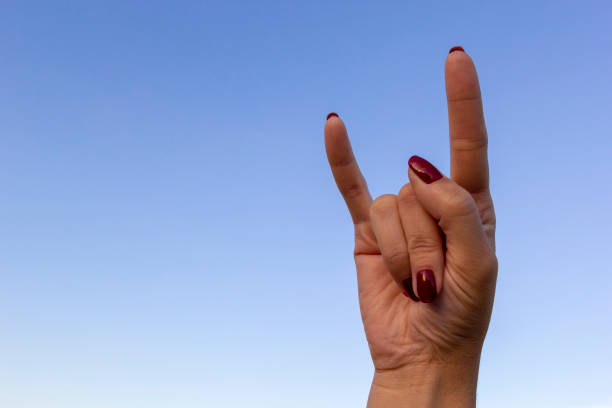 istock Hand gesturing rock & roll, heavy metal, devil horns gesture or I love you on blue sky background. 1162336408