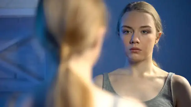 Teenage girl looking in bathroom mirror reflection in astonishment, insecurities