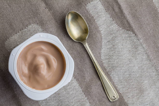 istock Chocolate yogurt pot wit small silver spoon, isolated on brown table cloth 1162338396