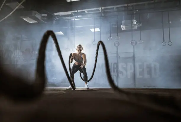 Young happy athletic woman having cross training with battle ropes in a health club. Copy space.