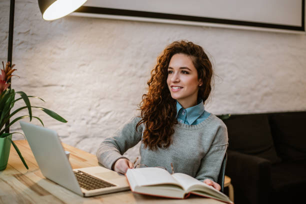 istock Thoughtful young woman reading book at the desk. 1162346480