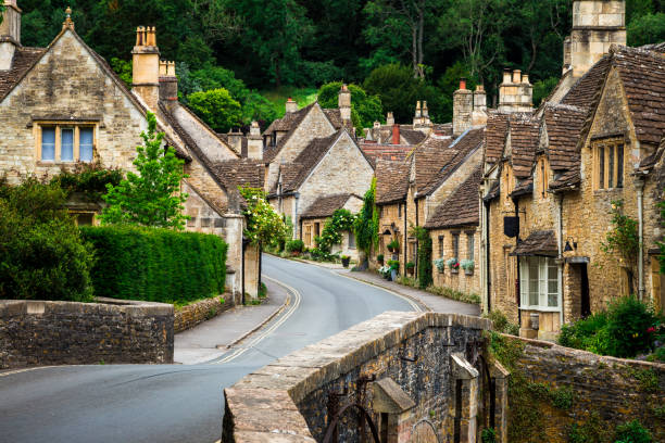 Traditional Idyllic English Countryside village with Cosy Cottages and narrow road Color image depicting a traditional English village in the Cotswolds area of southwest England. The cosy little brick cottages line the narrow road, and there is also a quaint bridge spanning a little stream. Room for copy space. wiltshire stock pictures, royalty-free photos & images
