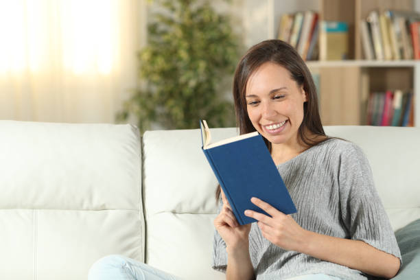 istock Happy woman reading a paper book sitting on a sofa 1162355941