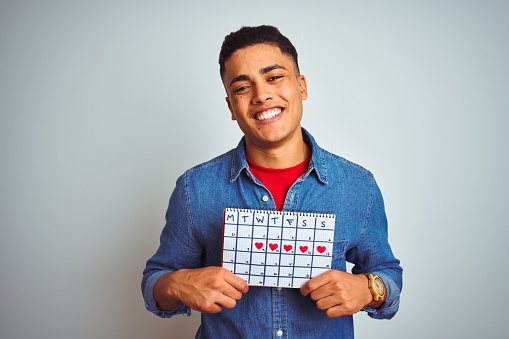 Young brazilian man holding calendar standing over isolated white background with a happy face standing and smiling with a confident smile showing teeth