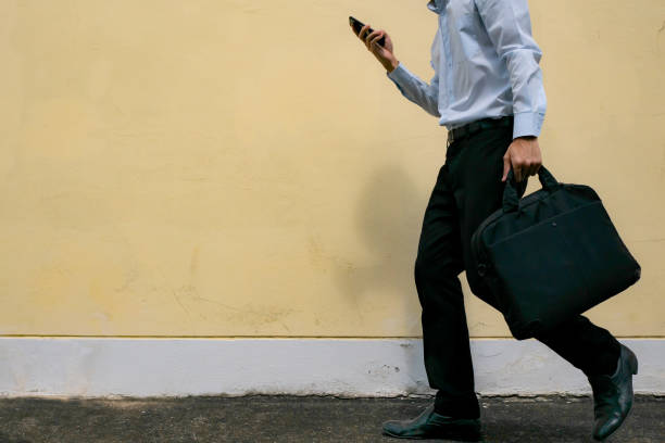 istock A man in formal outfit holding phone and laptop bag while walking to work 1162360262