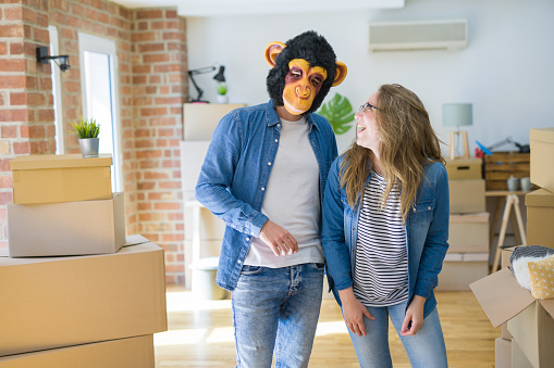 Young couple having fun wearing a monkey mask moving to a new apartment around cardboard boxes