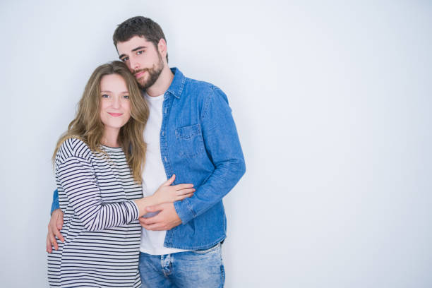 istock Young beautiful couple standing together over white isolated background with serious expression on face. Simple and natural looking at the camera. 1162360641