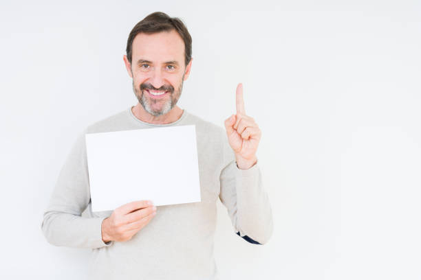 istock Senior man holding blank paper sheet over isolated background surprised with an idea or question pointing finger with happy face, number one 1162361031