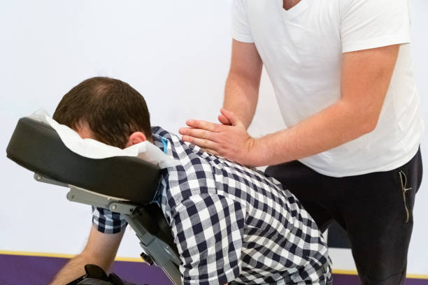 uomo seduto su una sedia da massaggio per il massaggio alla schiena. - chiropractor human spine office physical injury foto e immagini stock