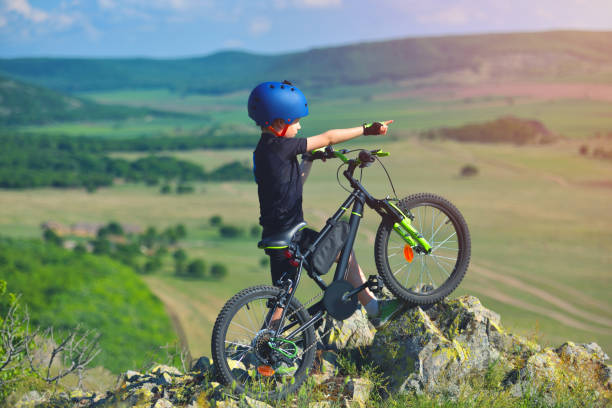 Little child stand next to his mountain bike on mountains edge and looks at the beautiful scenery stock photo