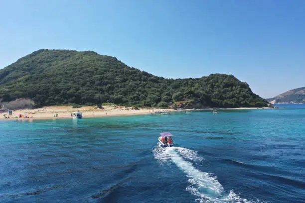 Photo of Small boat with tourists heading to iconic small uninhabited island of Marathonisi featuring clear water sandy shore and natural hatchery of Caretta-Caretta sea turtles, Zakynthos island, Ionian, Greece