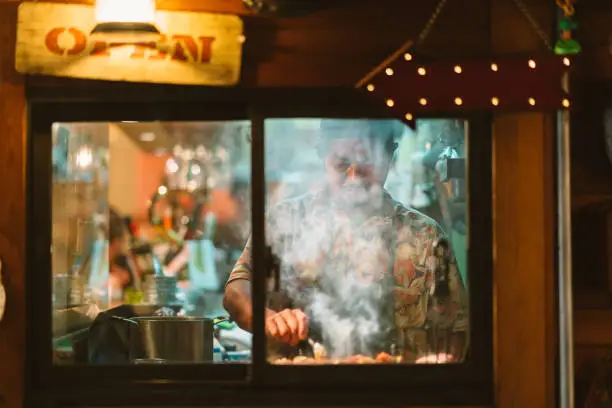 An owner of a Japanese style pub is cooking Japanese food in the kitchen of his shop.