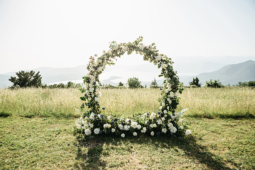 Beautiful wedding arch of flowers or white roses in a field or meadow. Preparation for a wedding event.