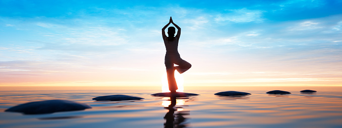 Young woman practicing yoga at a calm sea at sunrise in the morning