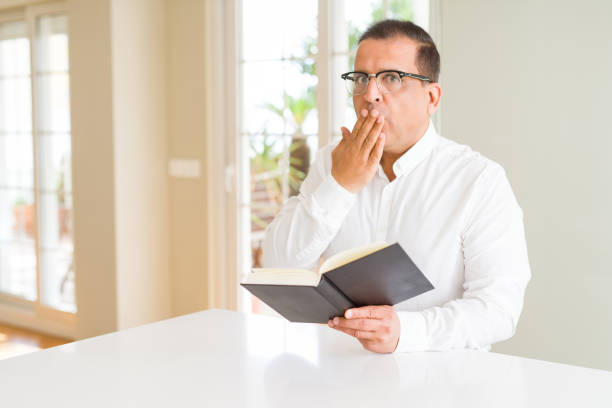 Middle age man reading a book at home wearing glasses cover mouth with hand shocked with shame for mistake, expression of fear, scared in silence, secret concept Middle age man reading a book at home wearing glasses cover mouth with hand shocked with shame for mistake, expression of fear, scared in silence, secret concept middle eastern ethnicity mature adult book reading stock pictures, royalty-free photos & images