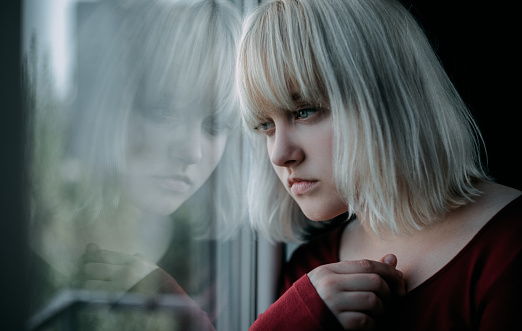 Primer plano de joven rubia deprimida cerca de la ventana en casa. Tristeza, nostlagic, depresión. photo