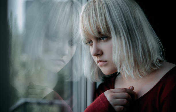 primer plano de joven rubia deprimida cerca de la ventana en casa. tristeza, nostlagic, depresión. - drug abuse addiction women violence fotografías e imágenes de stock