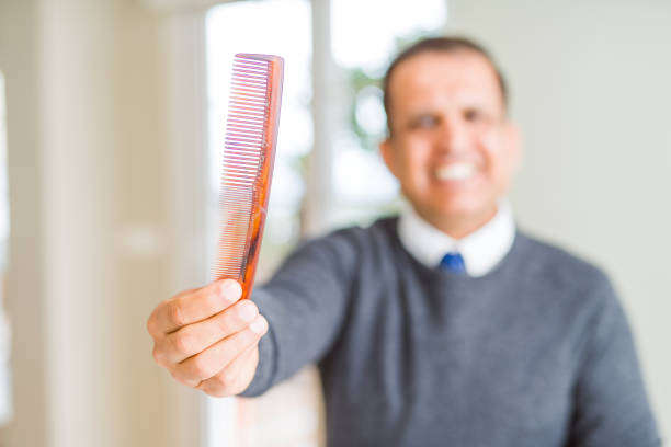 Middle age man holding and showing hair comb while smiling to the camera
