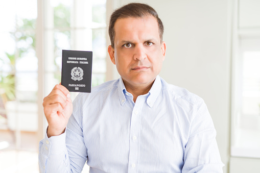 Middle age man holding holding passport of Italy with a confident expression on smart face thinking serious