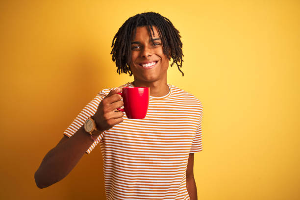 istock Afro american man with dreadlocks drinking a cup of coffee over isolated yellow background with a happy face standing and smiling with a confident smile showing teeth 1162385582