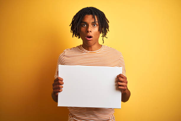 istock Afro american man with dreadlocks holding banner over isolated yellow background scared in shock with a surprise face, afraid and excited with fear expression 1162385597